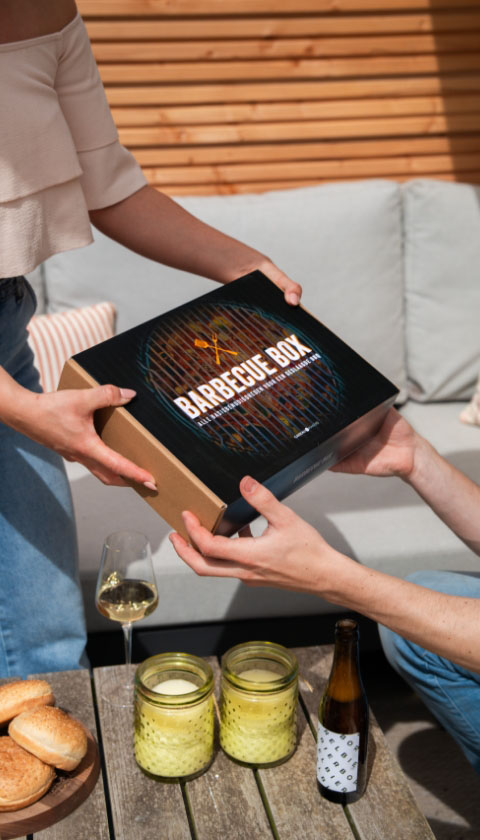 Vrouw overhandigt BBQ box cadeau op terras met wijn en broodjes