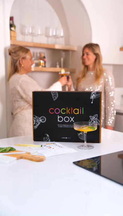 Cocktailbox op aanrecht met twee vrouwen die cocktails maken